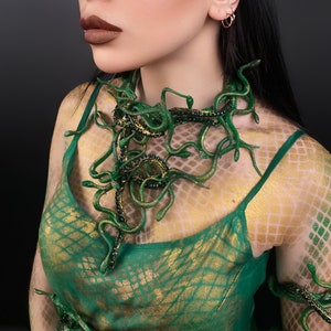 May include: A woman wearing a green and gold patterned dress with a snake-like necklace made of green plastic. The necklace is made up of many small snakes that are intertwined.