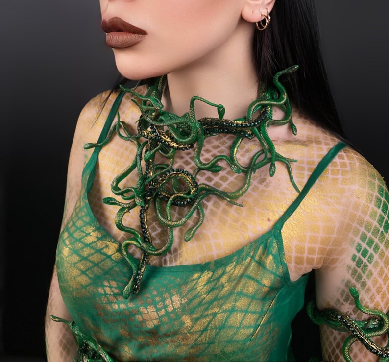 May include: A woman wearing a green and gold patterned dress with a snake-like necklace made of green plastic. The necklace is made up of many small snakes that are intertwined.