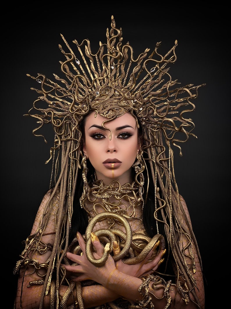 May include: A woman wearing a gold snake crown and a gold snake costume. The snakes are coiled around her arms and neck.