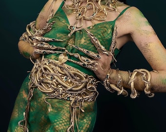 May include: A woman wearing a green dress with a gold snake-shaped belt and necklace. The dress has a snake skin pattern. The woman is also wearing gold snake-shaped bracelets.