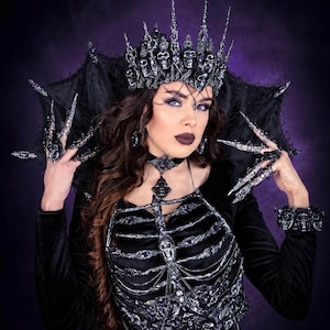May include: A gothic-themed ensemble featuring a black crown adorned with skulls and purple accents. The outfit includes a matching choker, skeletal bodice, and long, claw-like nail accessories. The overall aesthetic is dark and dramatic, set against a purple backdrop.
