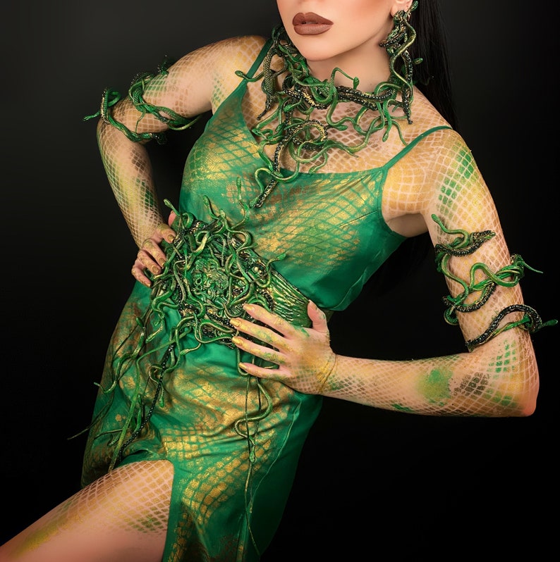 May include: A woman wearing a green dress with a snake-like design. The dress has a gold and green pattern and is decorated with snake-like jewelry. The woman's arms are also decorated with snake-like jewelry.
