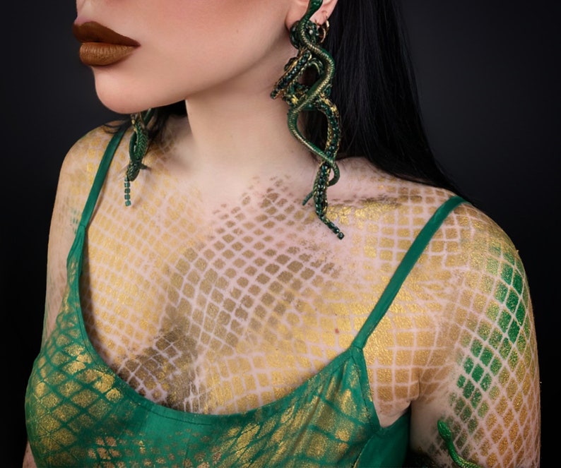 May include: A woman wearing a green top with a snake scale pattern. She is wearing large green snake earrings.