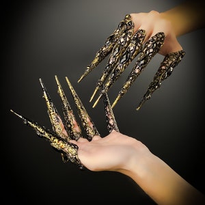 May include: A pair of black and gold finger rings with intricate designs and pointed tips, resembling claws.