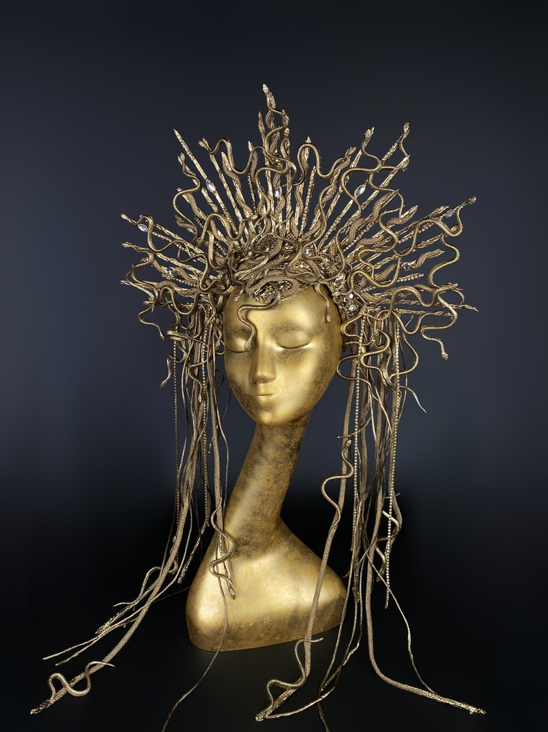 May include: A gold-colored headpiece with a crown of snakes and long, flowing strands of snakes. The headpiece is on a mannequin head.