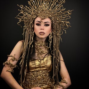 May include: A woman wearing a gold snake-themed costume with a crown, necklace, and bracelets. The costume is made of gold-colored fabric and features a snake design.