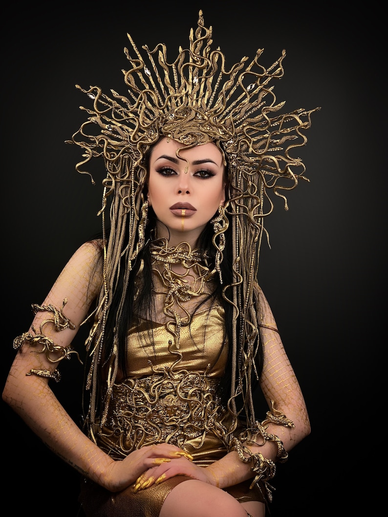 May include: A woman wearing a gold snake-themed costume with a crown, necklace, and bracelets. The costume is made of gold-colored fabric and features a snake design.