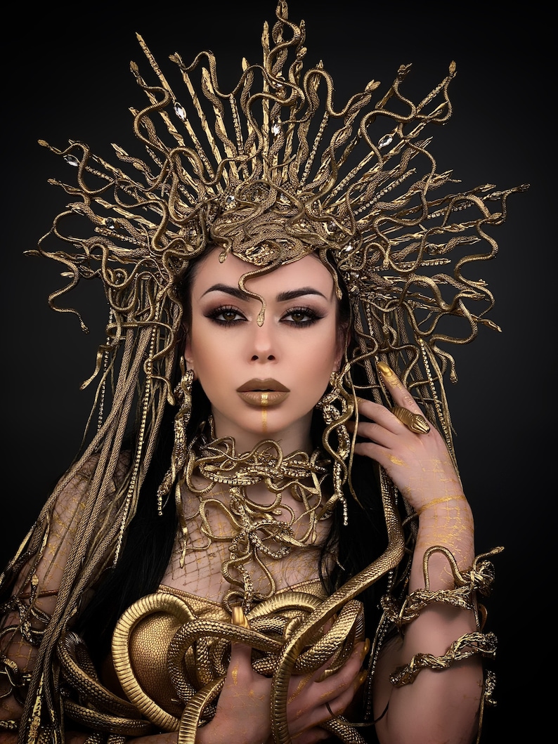 May include: A woman wearing a gold snake crown, necklace, and bracelets. The snakes are intertwined and form a decorative pattern. The woman has dark hair and is wearing gold makeup.