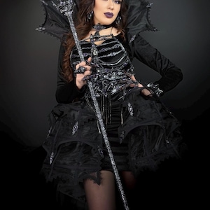 May include: A gothic-style costume featuring a black velvet dress with a structured bodice and layered skirt. The ensemble includes a matching crown, choker, and a decorative staff. The outfit is accented with silver embellishments and lace.