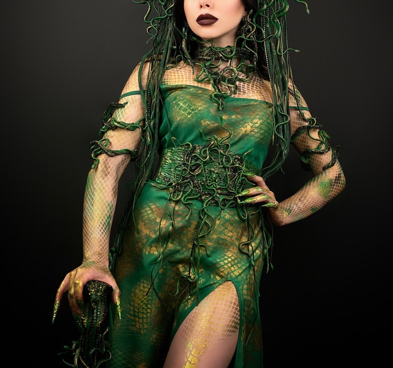 May include: A woman wearing a green and gold dress with a snake-like pattern. The dress has a high neckline and a fitted bodice. The woman is wearing a snake-like headpiece and has green makeup on her eyes and lips.