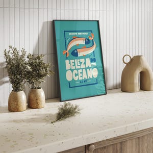 Almanac Co Prints blue poster featuring two colorful fish with the text 'Beleza do Oceano' in bold lettering, Portuguese style. Framed in modern kitchen.