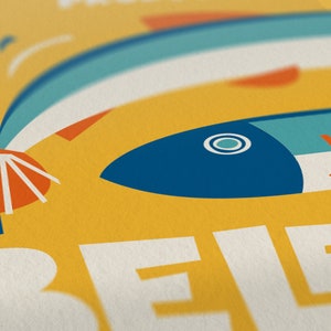 Close up of a bright yellow Almanac Co Prints poster featuring two colorful fish with the text "Beleza do Oceano" in bold lettering, Portuguese style.
