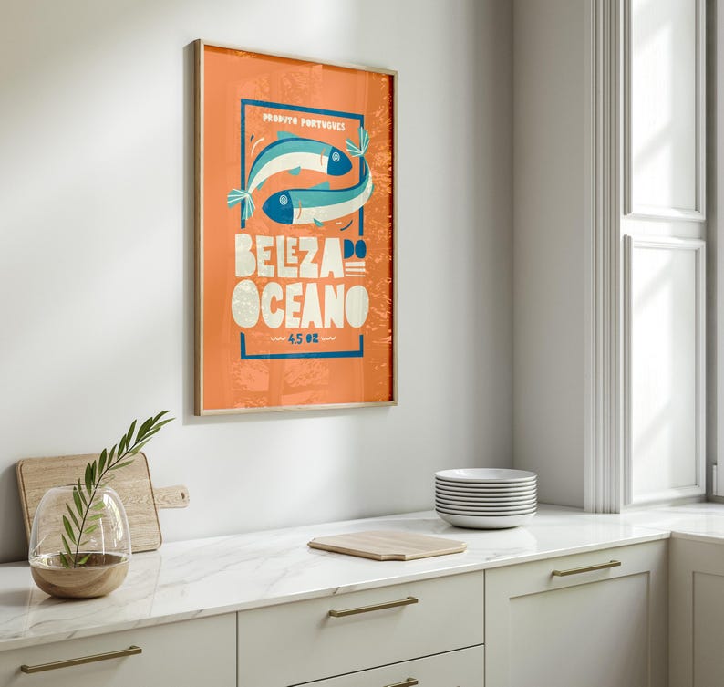 Almanac Co Prints orange poster featuring two colorful fish with the text 'Beleza do Oceano' in bold lettering, Portuguese style. Framed in modern white kitchen.