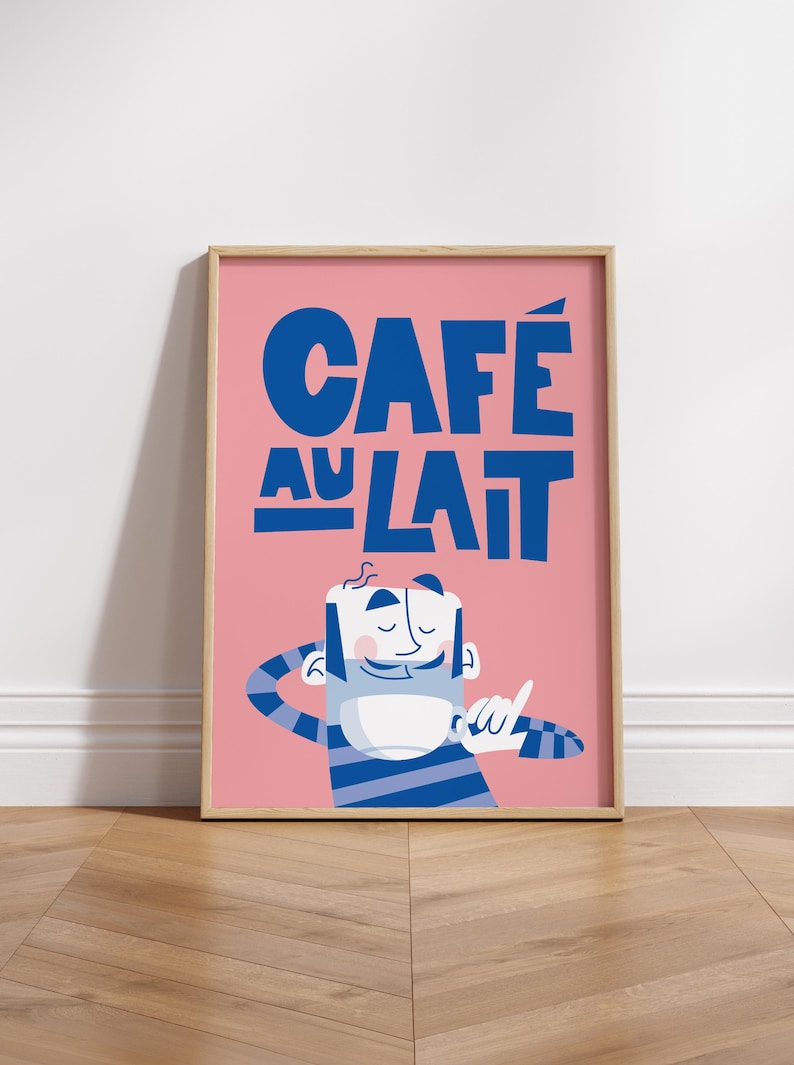 Almanac Co Prints framed 'Café au Lait' poster with bold blue text and a cheerful character, set against a pink background for fun kitchen decor. Framed on wooden floor