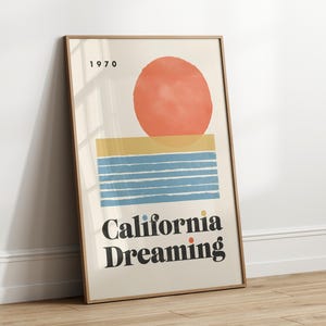 Almanac Co Prints framed poster titled 'California Dreaming' with a red sun, blue waves, and minimalist 1970s design, perfect for home decor. Framed leaning against white wall.