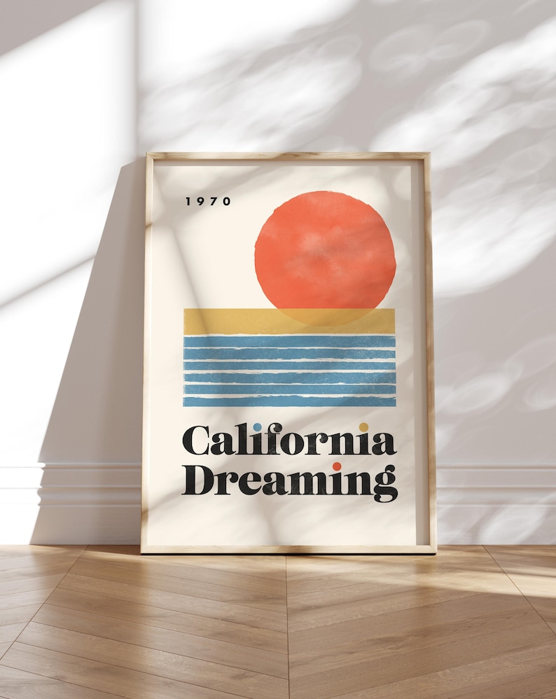 Almanac Co Prints framed poster titled 'California Dreaming' with a red sun, blue waves, and minimalist 1970s design, perfect for home decor. Framed leaning against white wall.