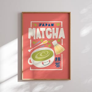 May include: A pink poster with a white frame featuring a cartoon illustration of a bowl of green matcha tea with a whisk and a spoon. The text "JAPAN MATCHA" is in a white box with a blue border. The text "抹茶" is in a red box with a white border.