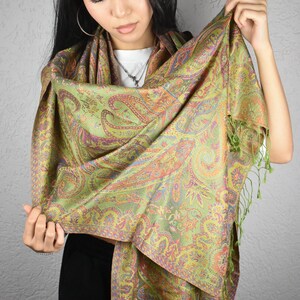 May include: A green paisley scarf with orange, purple, and yellow accents. The scarf has a detailed pattern and a fringe trim. The scarf is made of a soft, flowing fabric, perfect for adding a touch of elegance to any outfit.