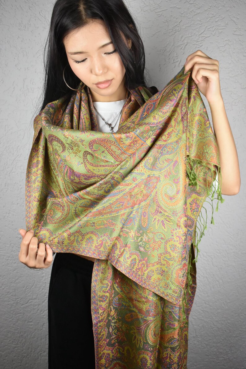 May include: A green paisley scarf with orange, purple, and yellow accents. The scarf has a detailed pattern and a fringe trim. The scarf is made of a soft, flowing fabric, perfect for adding a touch of elegance to any outfit.