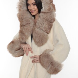 May include: A white fur coat with a brown fur collar and cuffs. The coat has a belt and a hood.