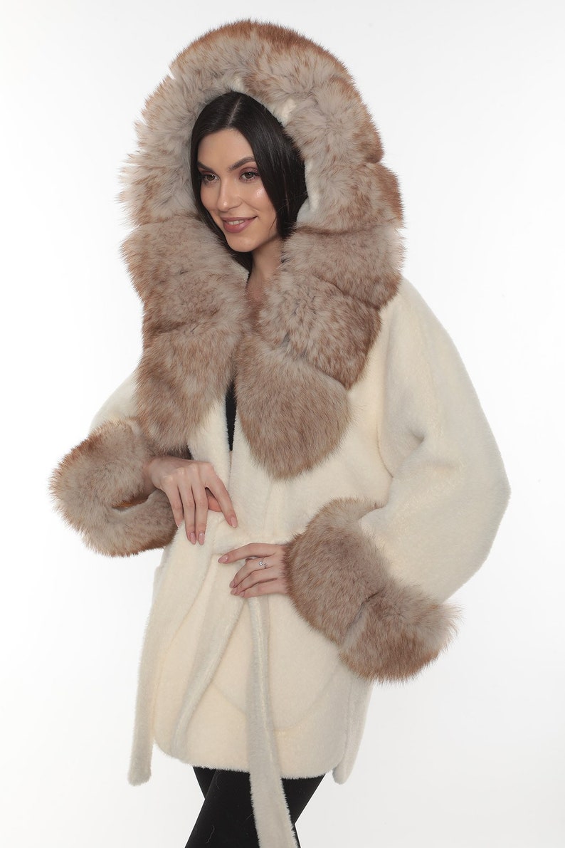 May include: A white fur coat with a brown fur collar and cuffs. The coat has a belt and a hood.