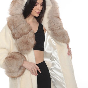May include: A white faux fur coat with a brown fur collar and cuffs. The coat has a hood and a tie belt.