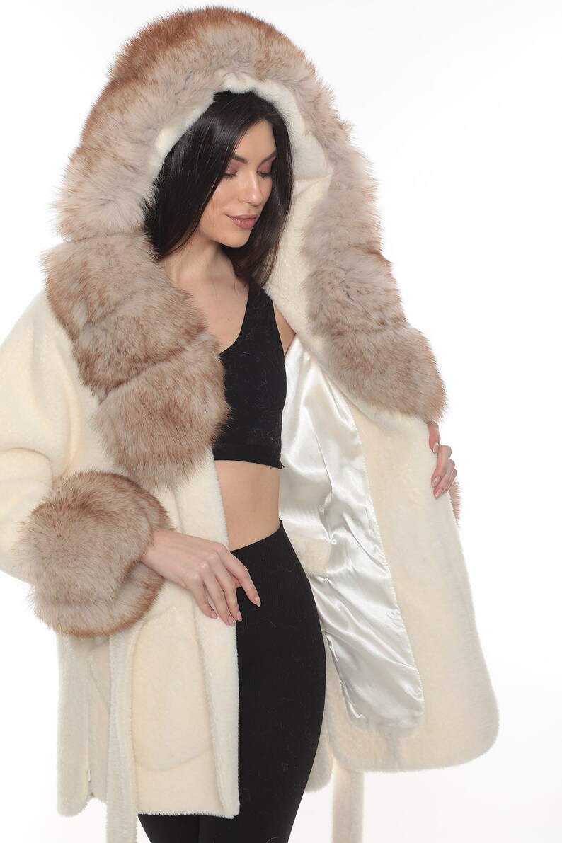 May include: A white faux fur coat with a brown fur collar and cuffs. The coat has a hood and a tie belt.