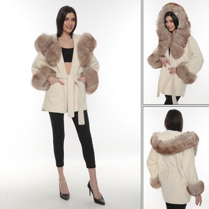 May include: A white faux fur coat with a brown faux fur trim around the hood and cuffs. The coat has a belt and two pockets.