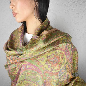 May include: A paisley patterned scarf in shades of green, orange, and purple. The scarf is draped over the shoulders, showcasing the intricate design. The fabric appears soft and flowing, suitable for a shawl or wrap.
