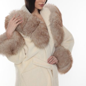 May include: A white faux fur coat with a brown fur collar and cuffs. The coat has a belt and a pocket on the front.