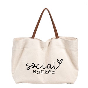 May include: A beige canvas tote bag with brown leather handles. The bag has the text "social worker" with a heart printed on it.