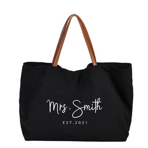 May include: Black canvas tote bag with brown leather handles. The bag has white text that says "Mrs. Smith EST. 2021".