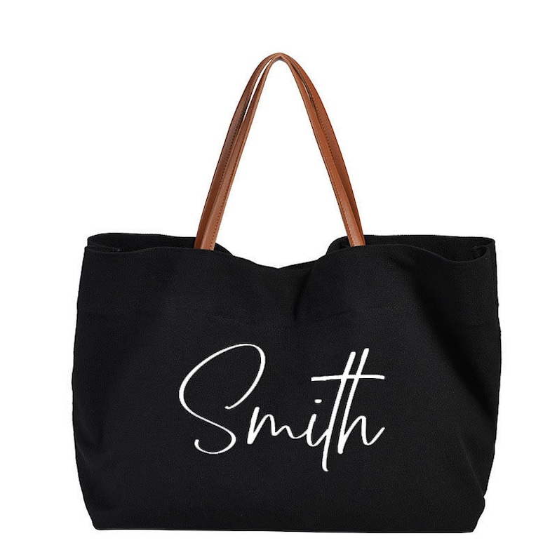 May include: Black canvas tote bag with brown leather handles and the word "Smith" written in white cursive on the front.