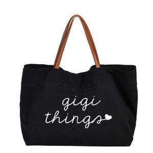 May include: Black canvas tote bag with brown leather handles. The bag has white text that says "gigi things" with a small white heart.