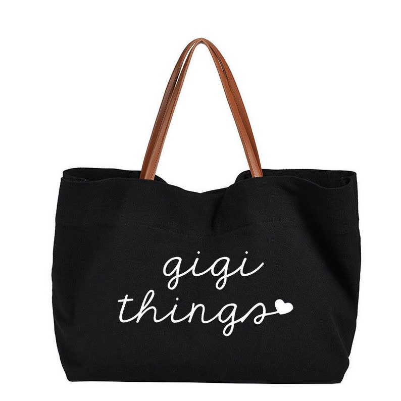 May include: Black canvas tote bag with brown leather handles. The bag has white text that says "gigi things" with a small white heart.