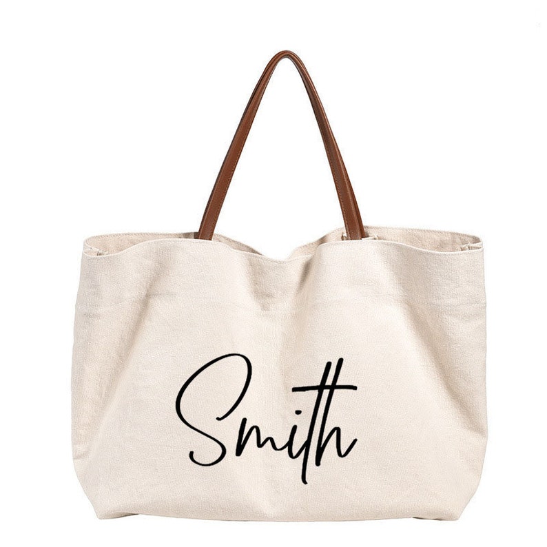 May include: A beige canvas tote bag with brown leather handles. The bag has the word "Smith" written in black cursive on the front.