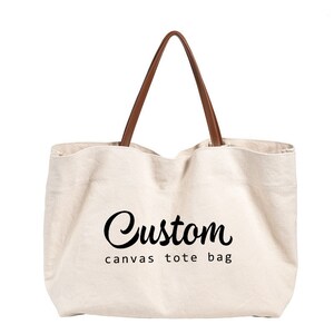 May include: A white canvas tote bag with brown leather handles. The bag has the text "Custom canvas tote bag" printed on the front.