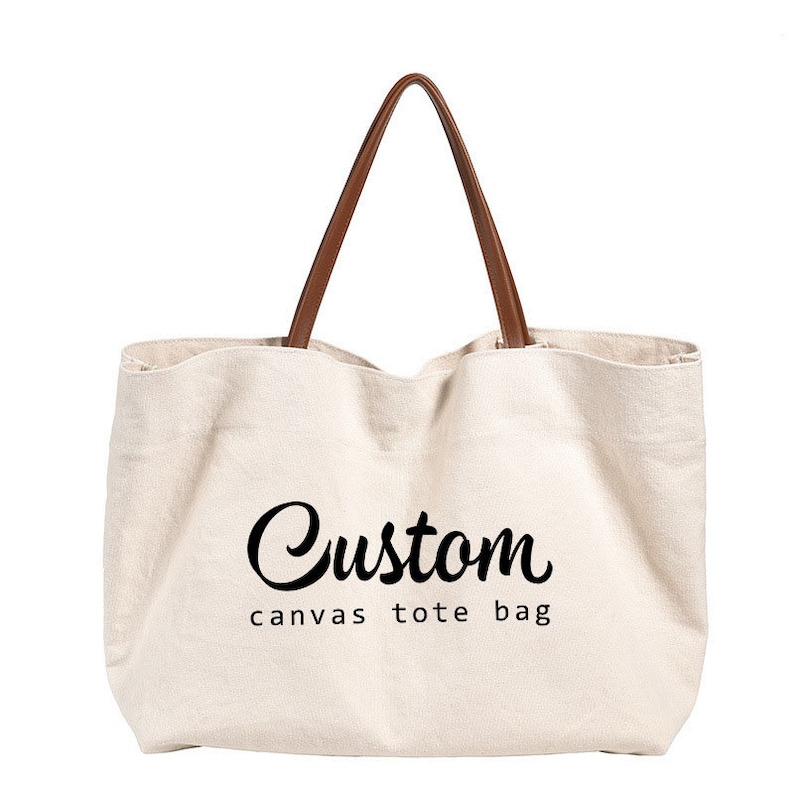May include: A white canvas tote bag with brown leather handles. The bag has the text "Custom canvas tote bag" printed on the front.