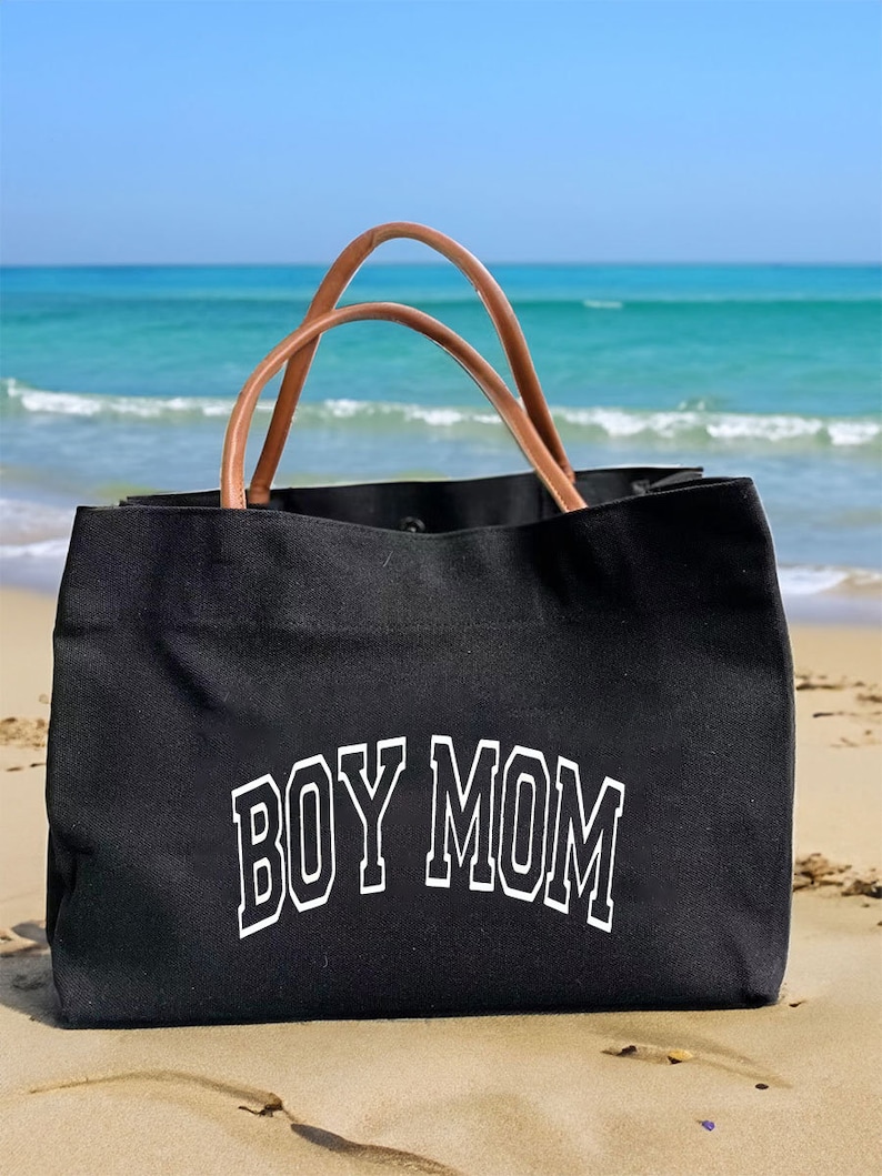 May include: Black canvas tote bag with brown leather handles. The bag has the text "BOY MOM" printed in white on the front.