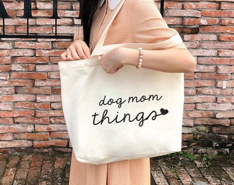 May include: A white canvas tote bag with black text that says "dog mom things" with a small heart symbol.
