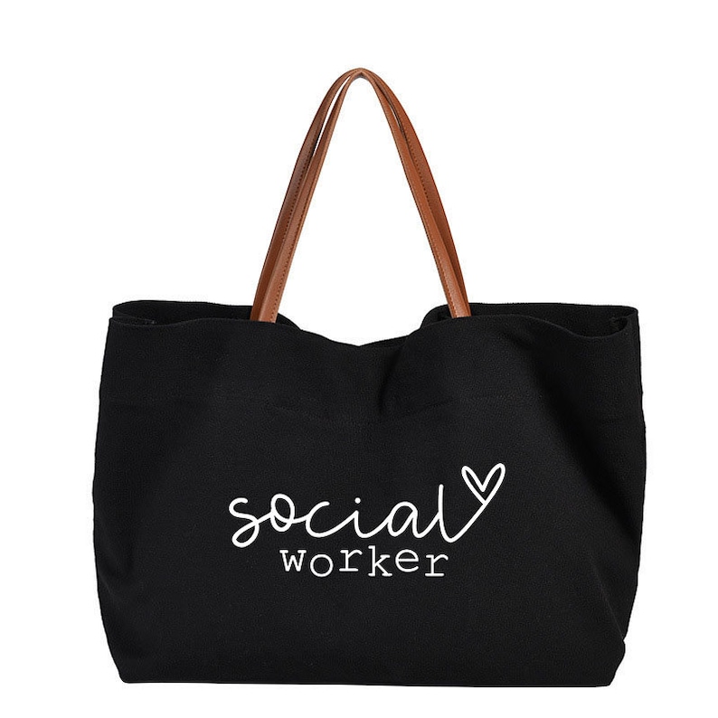 May include: Black canvas tote bag with brown leather handles. The bag has white text that says "social worker" with a heart symbol.