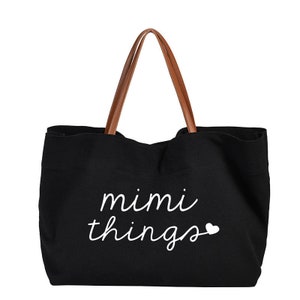 Op de afbeelding: Zwarte canvas tote bag met bruine leren handvatten en de tekst "mimi things" in wit met een klein wit hartje.