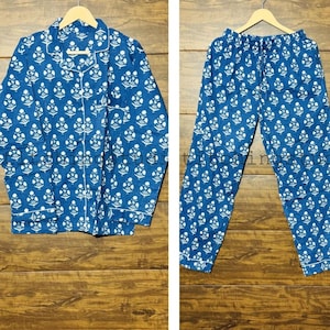May include: Blue and white floral print pajama set. The set includes a button-down shirt with a notched collar and long sleeves, and matching drawstring pants. The pajamas are displayed on a wooden surface.