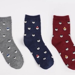 May include: Set of six pairs of socks with a penguin pattern. The socks are in various colors, including beige, gray, navy blue, burgundy, and yellow.