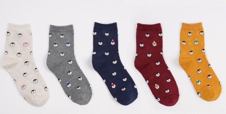 May include: Set of six pairs of socks with a penguin pattern. The socks are in various colors, including beige, gray, navy blue, burgundy, and yellow.