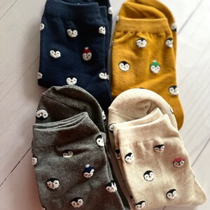 May include: Four pairs of socks with penguin designs. The socks are in navy blue, mustard yellow, gray, and cream.