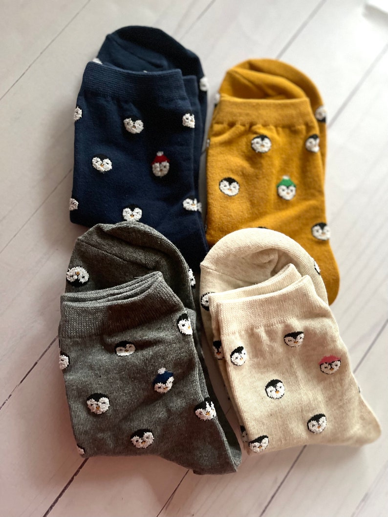 May include: Four pairs of socks with penguin designs. The socks are in navy blue, mustard yellow, gray, and cream.