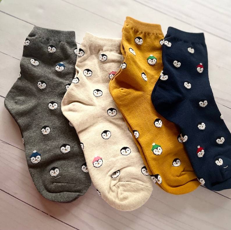 May include: Four pairs of ankle socks with a penguin pattern. The socks are in gray, beige, yellow, and navy blue.
