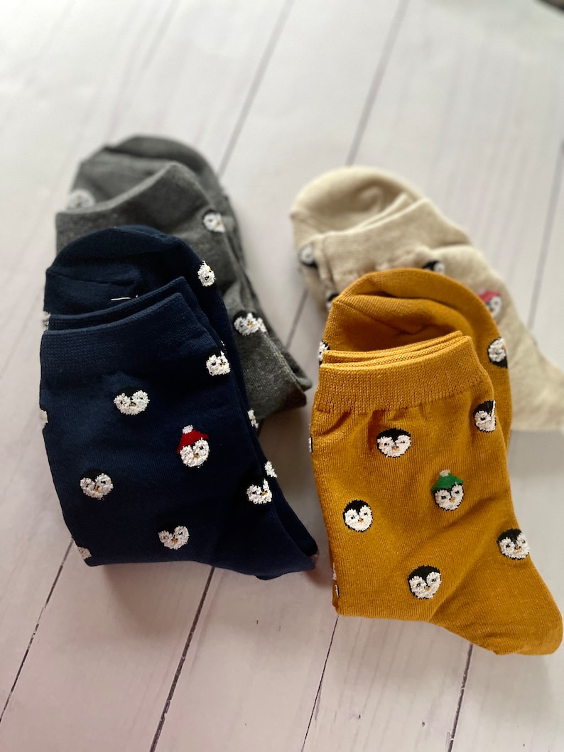 May include: Three pairs of socks with penguin designs. One pair is navy blue with white penguins, one pair is mustard yellow with white penguins, and one pair is gray with white penguins.