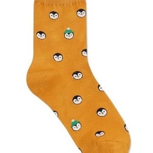 May include: A pair of yellow socks with a pattern of penguins wearing hats. Some penguins are wearing green hats.